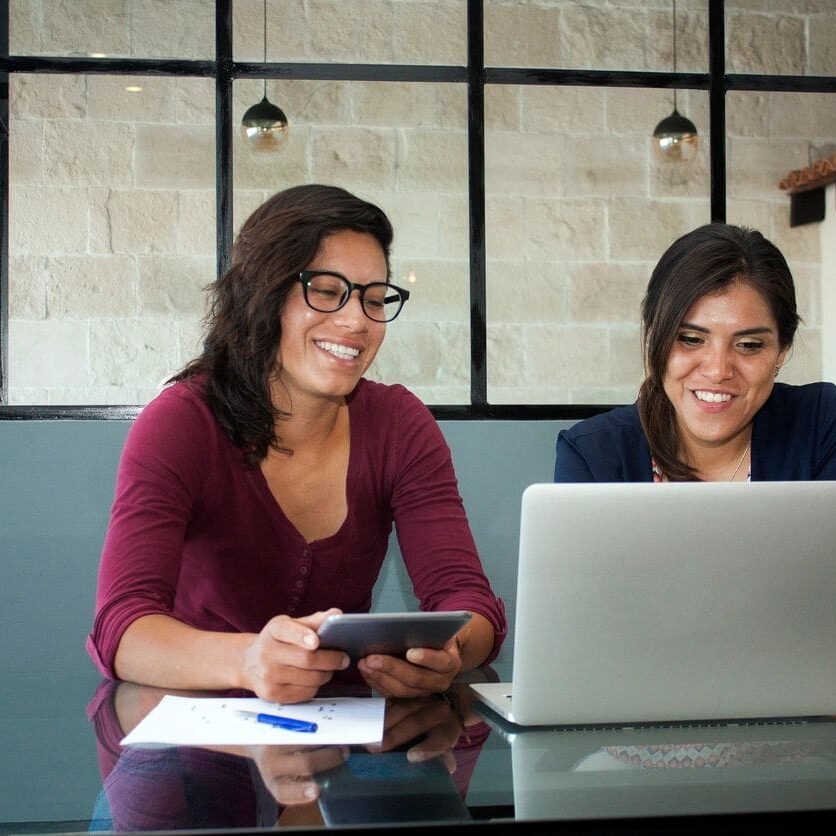 Two women sitting at a table looking at a laptop.